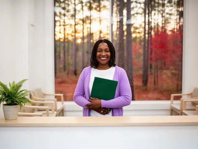 A clinic office manager holding a folder behind a reception counter.
